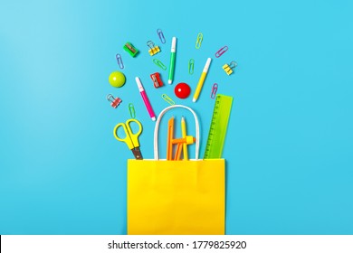 School Supplies In A Bright Yellow Paper Bag On A Blue Background. Back To School Concept. Concept Of Shopping In A Stationery Store. School Sale Concept. Top View, Flat Lay.