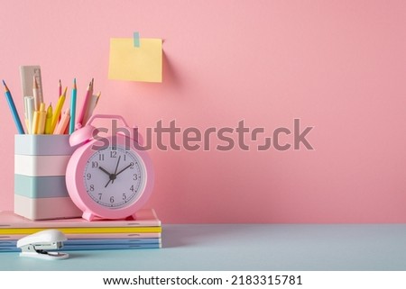 School supplies concept. Photo of stand for pencils alarm clock stack of notebooks stapler and sticky note paper attached to pink wall with empty space