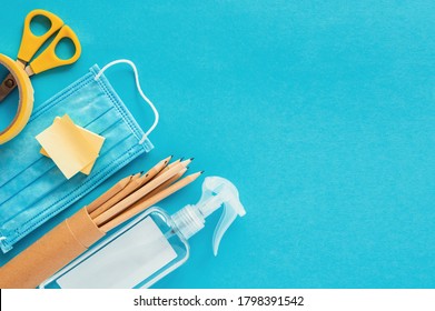 School Supplies And Coronavirus Prevention Items Top View On A Blue Paper Background. Back To School During Corona Virus Pandemic Concept