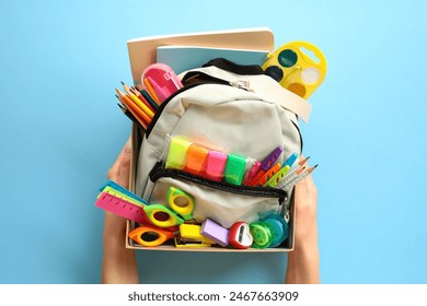 School supplies donation concept. Backpack with school supplies in cardboard box in women's hands on blue background