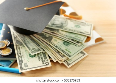 School supplies, graduation hat, dollar banknotes and coins on wooden table. Pocket money concept