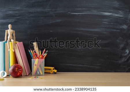 School supplies layout. Side view photo of desk setup with pencils organizer, ruler, books, red apple, mannequin body, and more on chalkboard background. Great for educational content or advertising