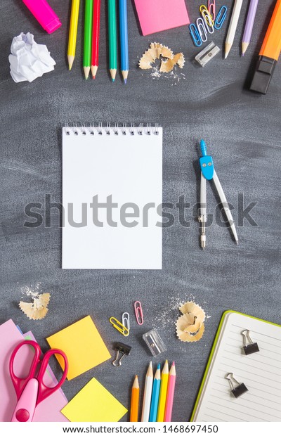 School supplies on a blackboard\
background. Notebook and dividers for right hand. Concept back to\
school. With copy space. Top view. Vertical\
layout