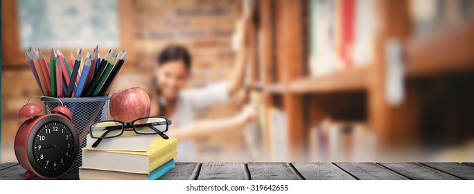 School Supplies On Desk Against Teacher And Little Girl Selecting Book In Library