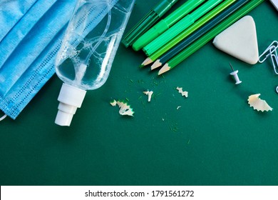 School supplies, protective mask and antiseptic on a green background