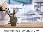 School supplies and schoolbag on wooden school desk. Blurred classroom background and copy space for school stuff and stationery on wooden desk. 