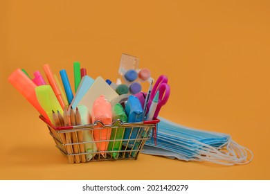 School Supplies In A Shopping Basket,medical Masks On Orange Background.Back To School During Coronavirus COVID-19 Pandemic.