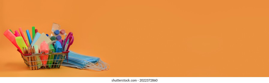 School Supplies In A Shopping Basket,medical Masks On Orange Background.Back To School During Coronavirus COVID-19 Pandemic. Copy Space. Banner