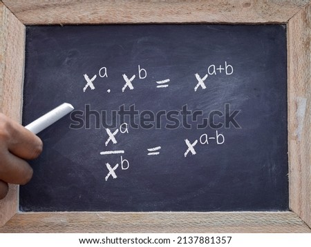School teacher hand holding chalk teaching mathematics exponent rules on chalkboard. 