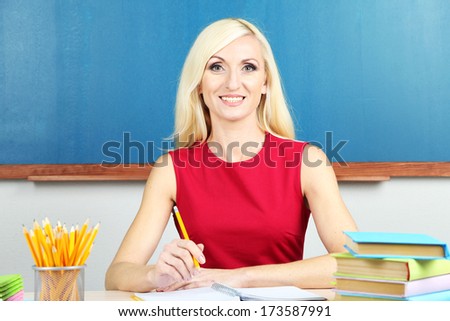 School teacher sitting at table on blackboard background