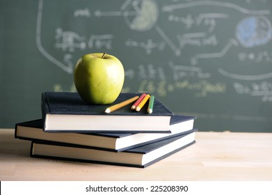 A school teacher's desk with stack of exercise books colored pencils and green apple. A green blackboard  - Powered by Shutterstock