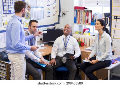 School Teachers Gather In A Small School Office For A Chat. They Look Happy. A Woman And Three Men Group Together.