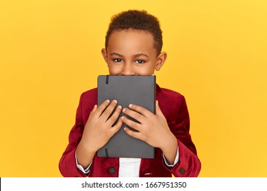 School, textbook and stationary items concept. Portrait of handsome Afro American boy having playful eyes covering face with black copy book. black pupil posing isolated holding diary, keeping secret