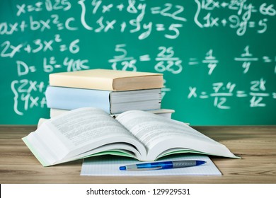 School Textbooks On A Desk In Front Of Blackboard