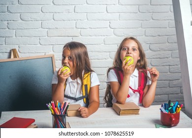 School Time Of Girls. Friendship Of Small Sisters In Classroom At Knowledge Day. Happy School Kids At Lesson In September 1. Back To School And Home Schooling. Little Girls Eat Apple At Lunch Break.