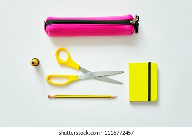 School Tools Such As Yellow Scissors, Pencil, Ruler, Eraser, And Pencil Case, Over A White Flatlay In Blue From Above