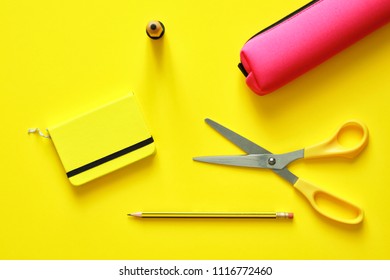 School Tools Such As Yellow Scissors, Pencil, Ruler, Eraser, And Pencil Case, Over A Yellow Flatlay In Blue From Above