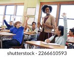 School, tutor and students raise their hands to ask or answer an academic question for learning. Diversity, education and primary school kids speaking to their woman teacher in the classroom.