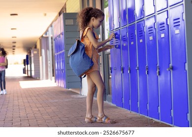 In school, two biracial female students opening lockers outdoors. Both have curly brown hair, one wearing orange dress and sandals, unaltered - Powered by Shutterstock