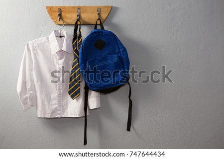 School uniform and schoolbag hanging on hook against wall