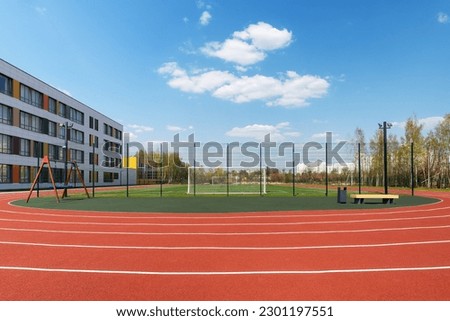 In the school yard: an red artificial turf running track and a soccer field with football goals