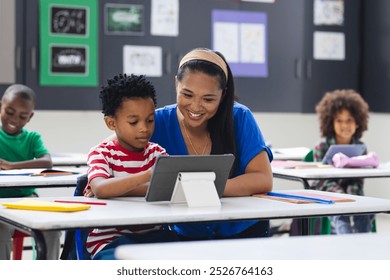 In school, young African American boy and woman are looking at a tablet in the classroom. He has short curly hair, she wears a blue top, both smiling, unaltered. - Powered by Shutterstock