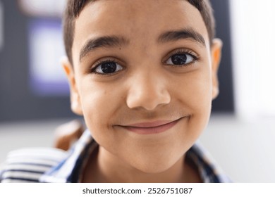 In school, young biracial boy with short dark hair and brown eyes is smiling in the classroom. Wearing a striped shirt, he looks happy and curious, unaltered. - Powered by Shutterstock