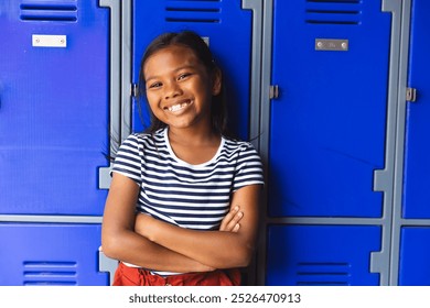 In school, young biracial female student is standing outdoors, arms crossed, smiling. She has brown skin, dark hair, and is wearing a striped top and red skirt, unaltered. - Powered by Shutterstock