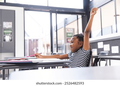 In school, young biracial girl with dark hair raising hand in the classroom, with copy space. Wearing a striped shirt, surrounded by notebooks and pencils, unaltered - Powered by Shutterstock