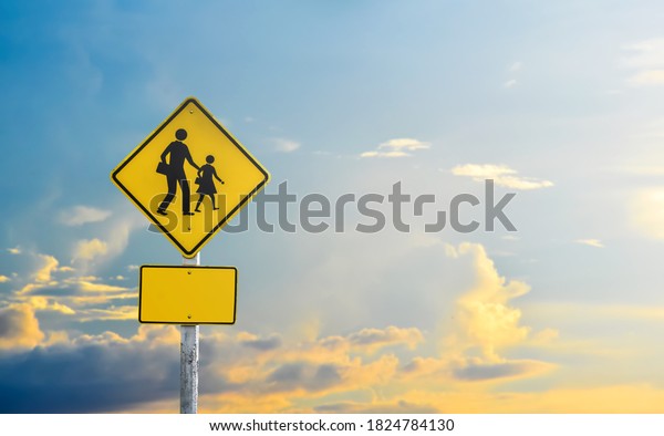 School zone ahead sign\
isolated on cloudy bluesky background with the light of the Sunset\
behind.
