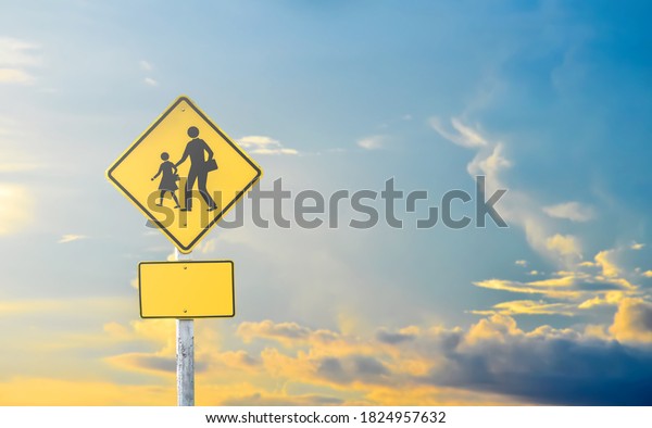 School zone ahead sign\
isolated on cloudy bluesky background with the light of the Sunset\
behind.