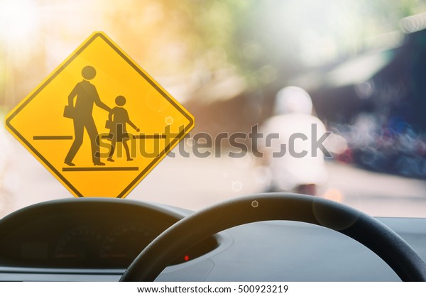 School zone warning sign and inside car view\
,steering wheel on blur traffic road with colorful bokeh light\
abstract background. Copy space of transportation and travel\
concept. Vintage tone\
color.