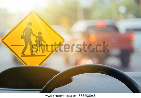 School zone warning sign and inside car view ,steering\
wheel on blur traffic road with colorful bokeh light abstract\
background. Copy space of transportation and travel concept.\
Vintage tone color. 