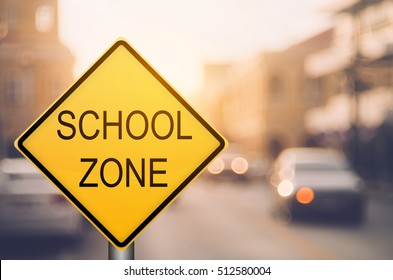 School Zone Warning Sign On Blur Traffic Road With Colorful Bokeh Light Abstract Background. Copy Space Of Transportation And Travel Concept. Vintage Tone Filter Color Style.