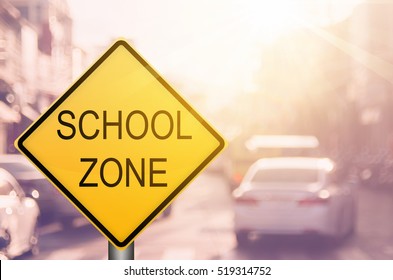 School Zone Warning Sign On Blur Traffic Road With Colorful Bokeh Light Abstract Background. Copy Space Of Transportation And Travel Concept. Vintage Tone Filter Color Style.