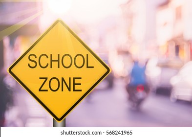 School Zone Warning Sign On Blur Traffic Road With Colorful Bokeh Light Abstract Background. Copy Space Of Transportation And Travel Concept. Vintage Tone Filter Color Style.