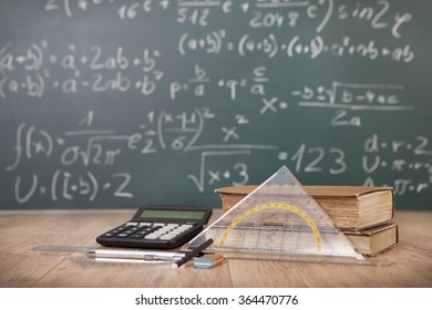 Schoolbooks and calculator lying on a wooden school desk in front of a green chalkboard with Mathematical formulas school - Powered by Shutterstock