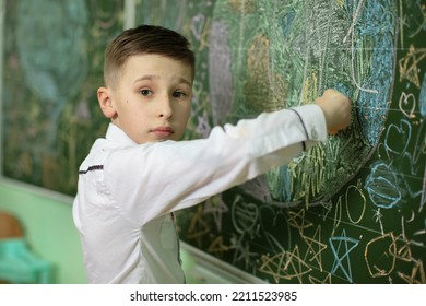 The Schoolboy At The Blackboard Draws With Chalk. Middle School Age. The Boy Is In The Classroom.