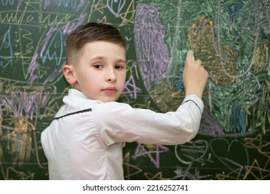 The Schoolboy At The Blackboard Draws With Chalk. Middle School Age. The Boy Is In The Classroom.