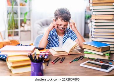 schoolboy boy sees poorly, tries to read through glasses. The child is sitting at home at his desk and reading a book. Back to school. Problems with the eyes. Poor eyesight