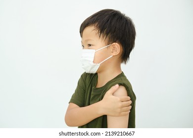 Schoolboy Child After Getting A Vaccine. Little Kid Wearing Medical Mask Showing His Arm With Bandage After Receiving Vaccination, Got Side Effect Pain At Arm, COVID 19 Vaccine For Children And Youth