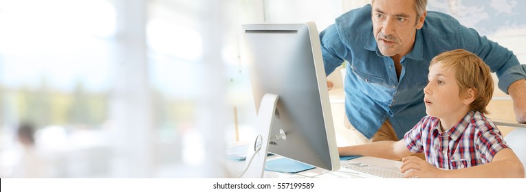 Schoolboy In Computer Lab With Teacher Helping