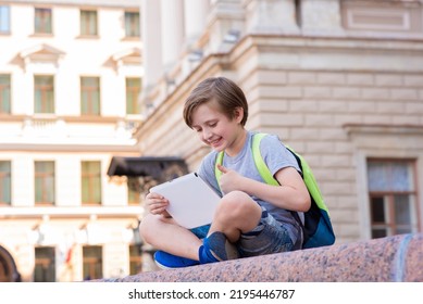 Schoolboy Is Engaged Using A Tablet Outside. The Child Watches Lectures From Anywhere In The World, Learns While Traveling Online, Remotely, In Correspondence Or Family Education Via The Internet.