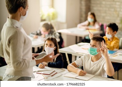 Schoolboy With Face Mask Raising Hand To Answer The Question During A Class In The Classroom. 