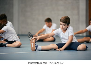 Schoolboy and his friends doing relaxation exercises and warming up for physical activity class at school gym. 