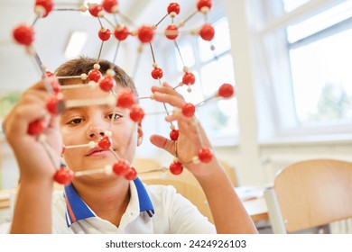 Schoolboy holding molecular structure while sitting in classroom at elementary school