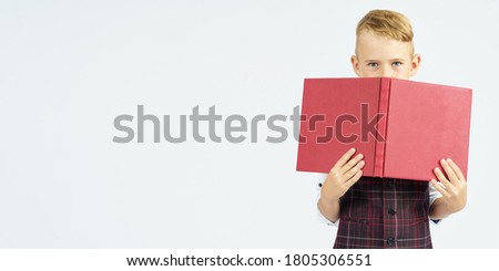 The schoolboy holds books, hiding his face behind them. Isolated background. Education concept