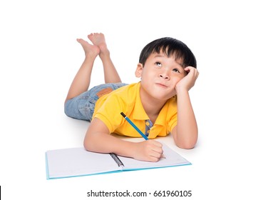 Schoolboy lying on a floor, looking up and writing in notebook.