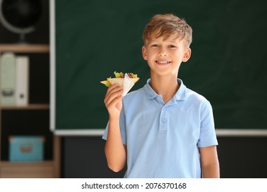 Schoolboy With Sandwich Against Blurred Background In School