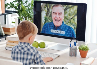 Schoolboy Sitting At Desk At Home When Having Online Class And Listening To Senior Science Teacher